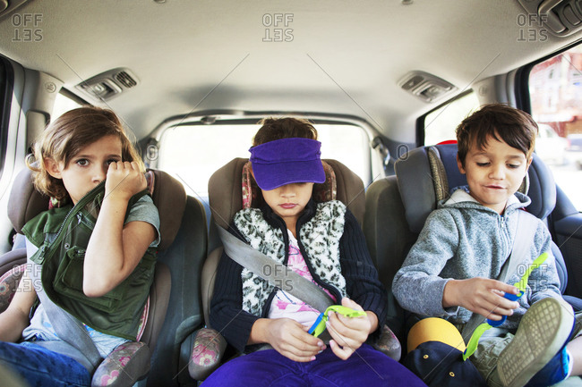 Three children strapped in car seats across the back seat of vehicle