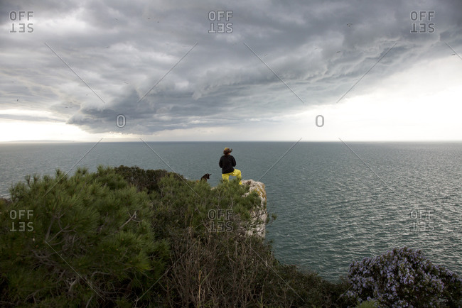 Woman standing on a bluff with her dog overlooking the Mediterranean Sea