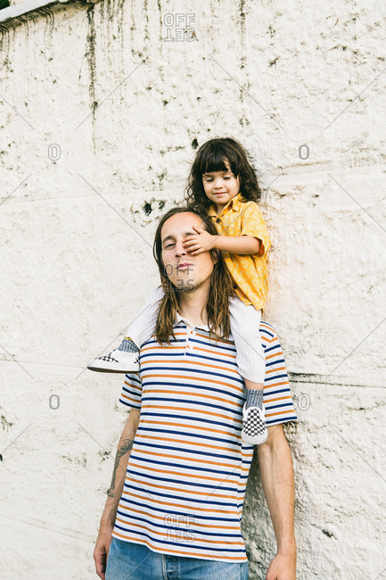 Child playfully covers father's eye while sitting on his shoulders