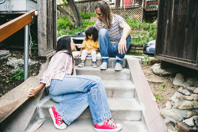 Family of three seated on steps in front of their home