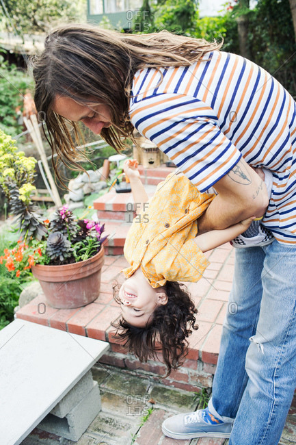 Man playfully hangs child upside down in garden