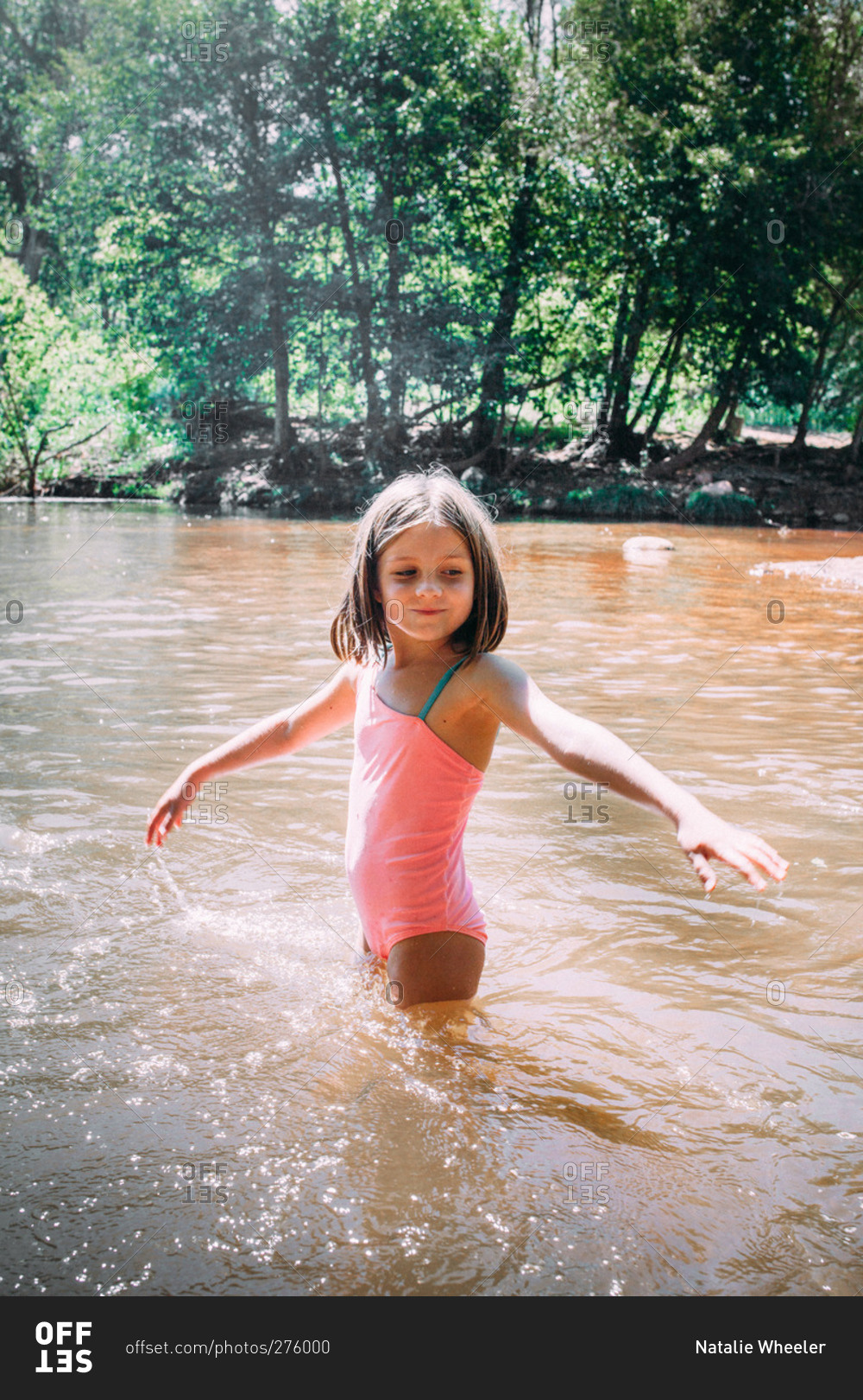 Girl standing in a river with arms raised stock photo OFFSET