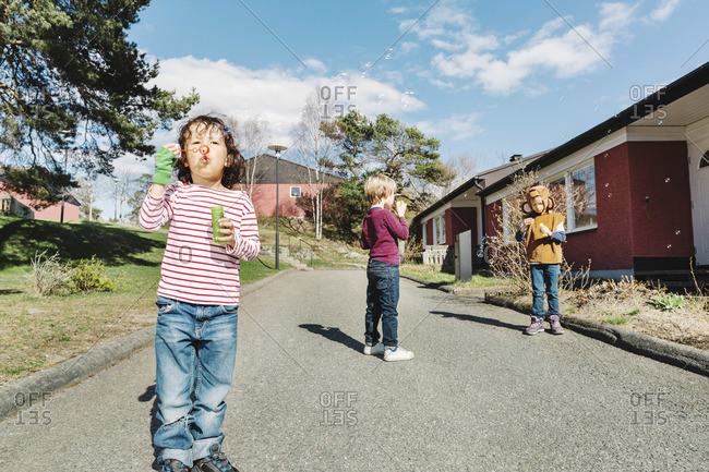 Friends playing with bubble wands on footpath in a yard