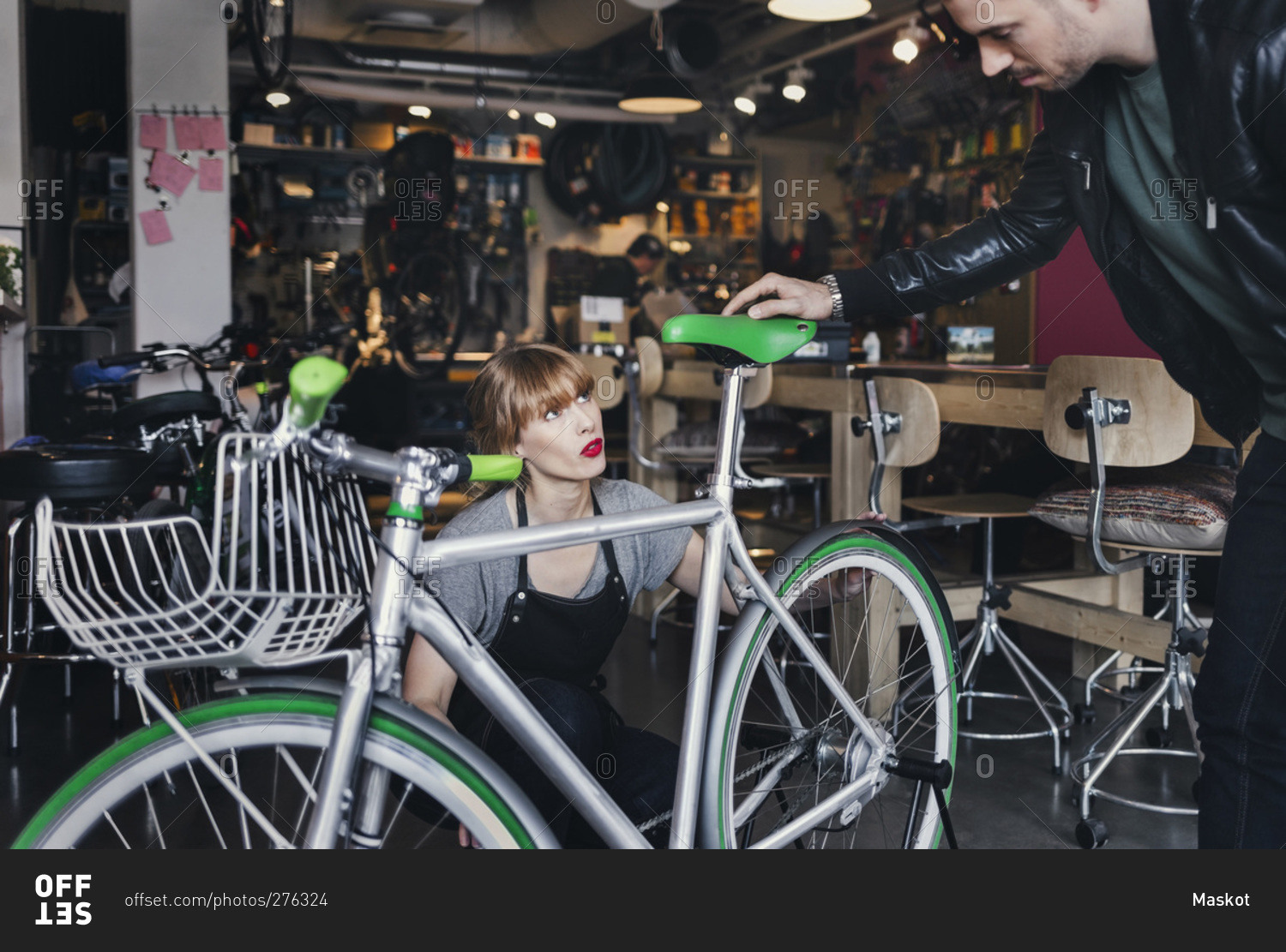 Female mechanic analyzing bicycle while talking to male customer in repair shop