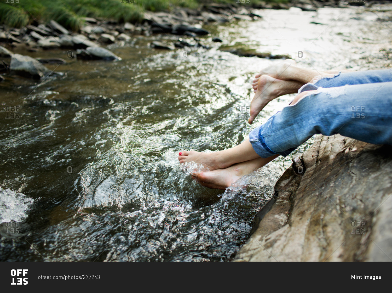 A woman in fashionable jeans with a rip, with her feet in the cool flowing waters of a river