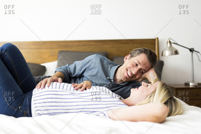 Husband looking adoringly at his pregnant wife lying on a bed