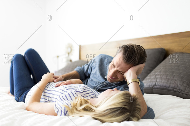Husband looking adoringly at his wife lying on a bed