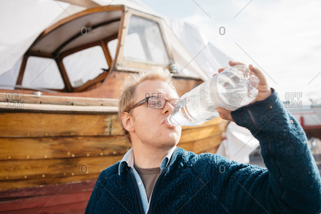Man drinking from water bottle by boat
