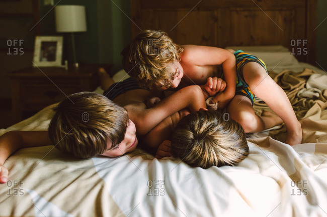 Three boys wrestling on a bed