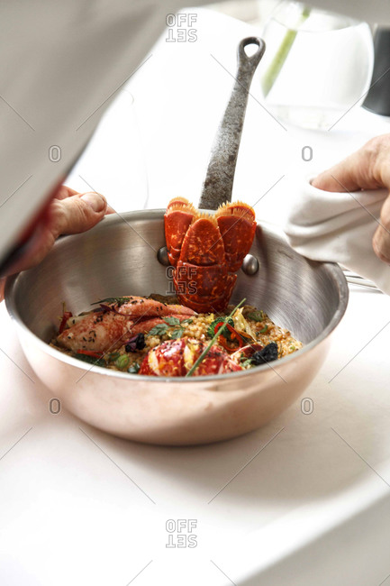 Hands wiping the lid of a pot with a seafood dish