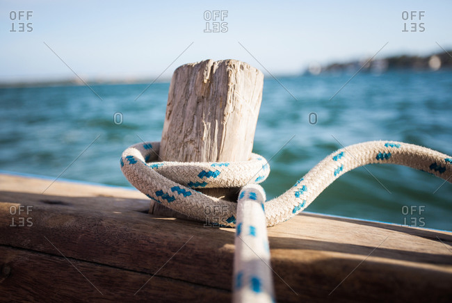 A rope wrapped around an old wood peg on a wooden sailboat adrift in blue water