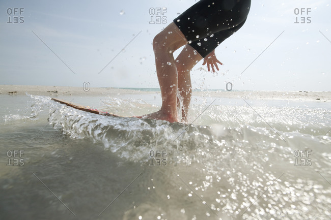 An action shot of a boy on a skim board at the shoreline