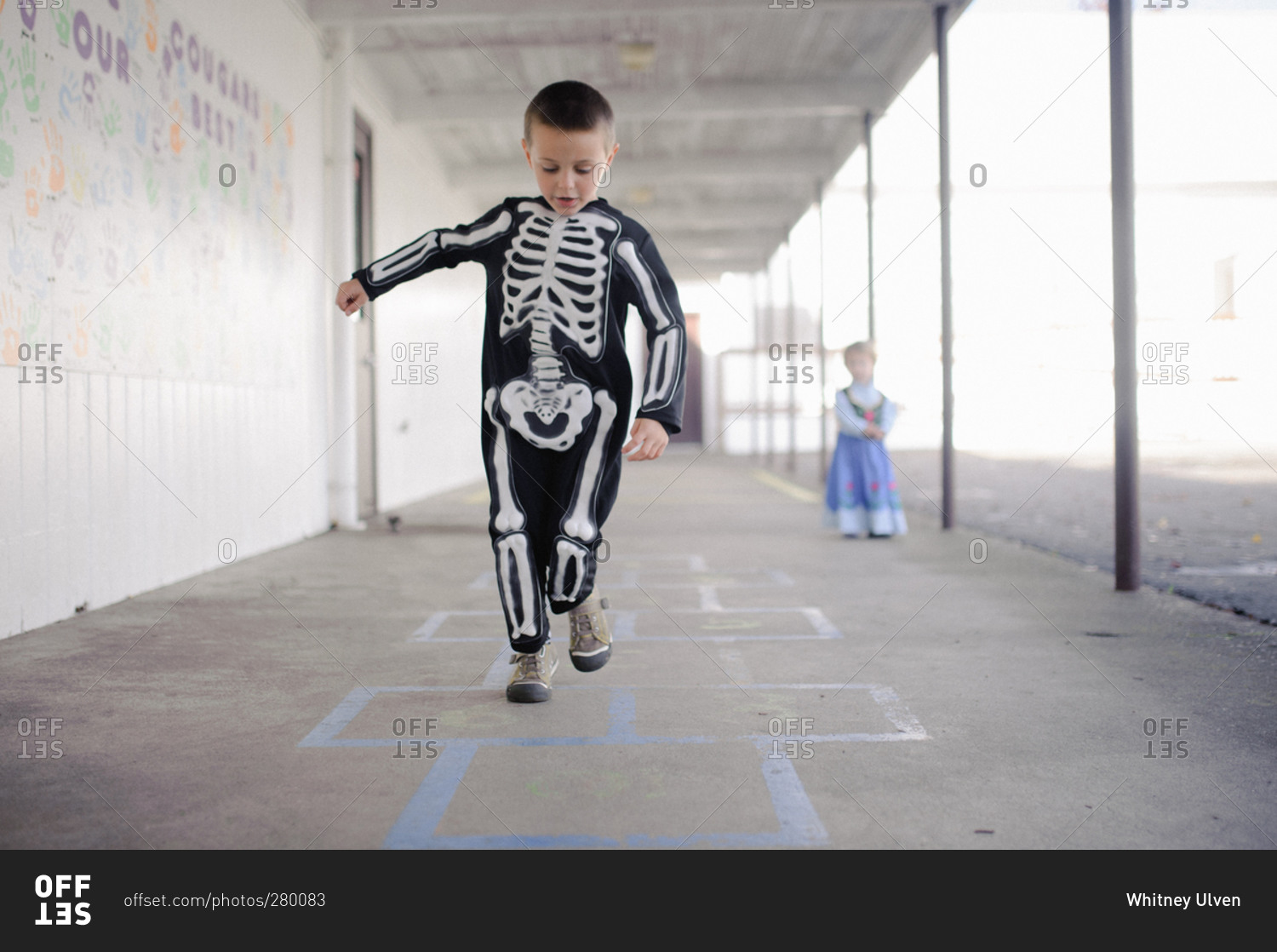 Little boy playing hopscotch dressed as skeleton for Halloween
