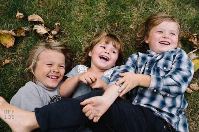 Three playful young siblings rolling around on grass