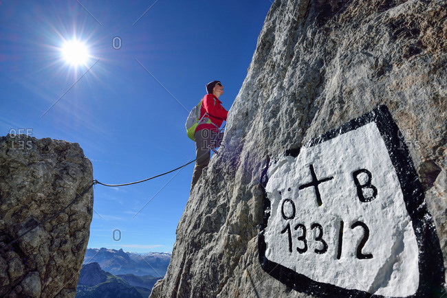 Woman ascending on fixed rope route to Hohes Brett, boundary mark in foreground, Hoher Goell, Berchtesgaden National Park, Berchtesgaden Alps, Upper Bavaria, Bavaria, Germany