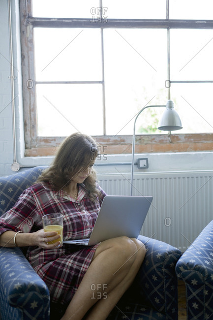 Woman drinking orange juice and using a laptop