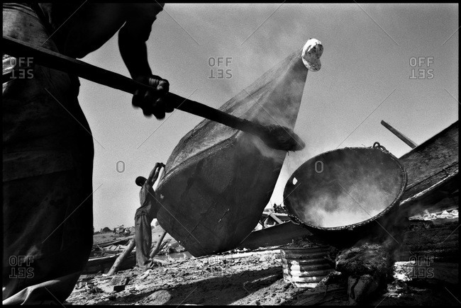 Man heating tar for boat repair, Mali