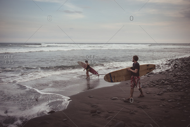El Zonte, El Salvador - June 3, 2015: Man and woman carrying surfboards on beach