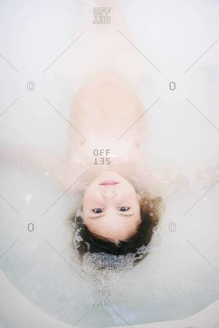 Young child lying in soapy water of bathtub
