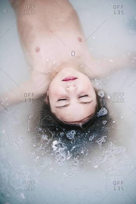 Young child relaxing in soapy water of bathtub