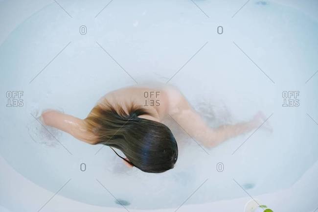 Young girl playing in soapy water in large bathtub