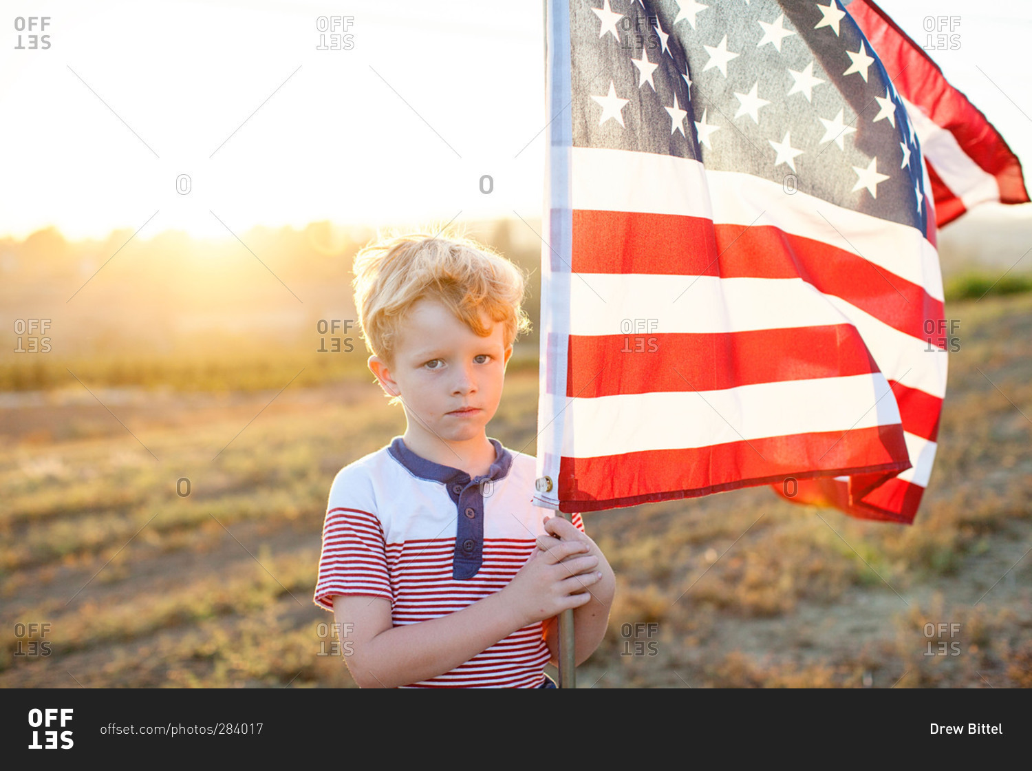 Boy in rural field holding American flag stock photo - OFFSET