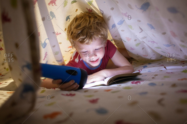 Boy reading under covers with a flashlight