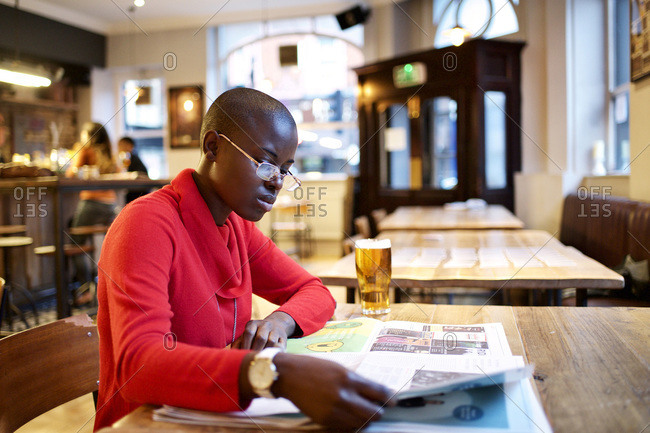 Woman reading newspaper over a beer