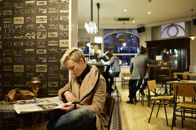 Woman reading newspaper in solitude at bar
