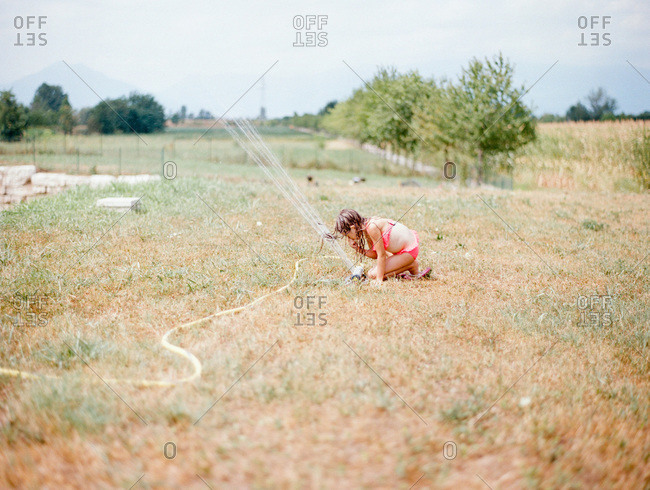 Little girl putting face in the sprinkler water