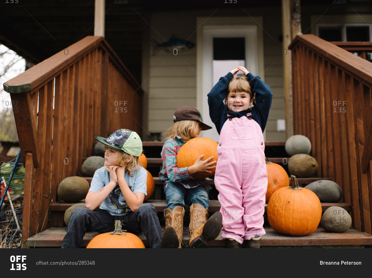 Three young siblings on front steps with pumpkins