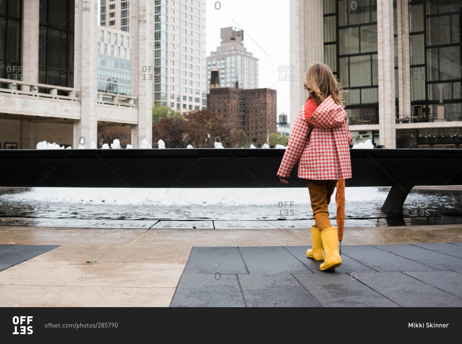 Girl in rain clothing standing by fountain