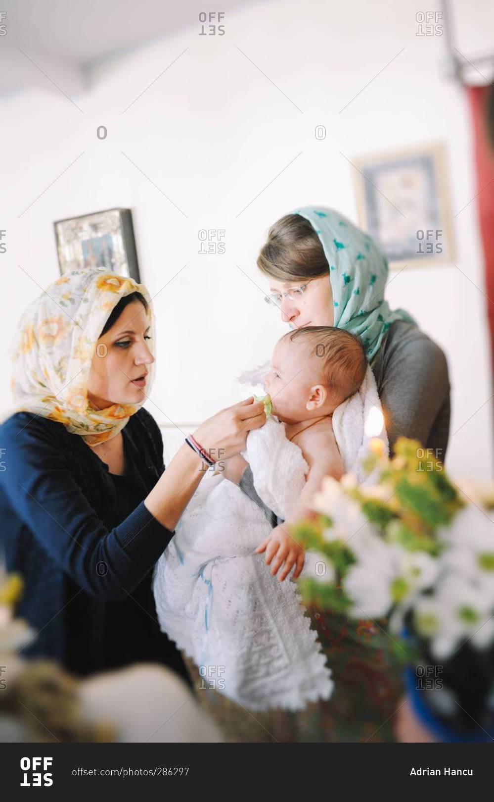 Godmother holding boy during Orthodox Christian Baptism while his mother gives him a pacifier in Chisinau, Moldova