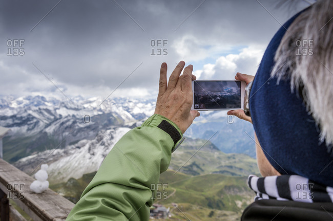 Senior woman taking cell phone picture from summit of Nebelhorn