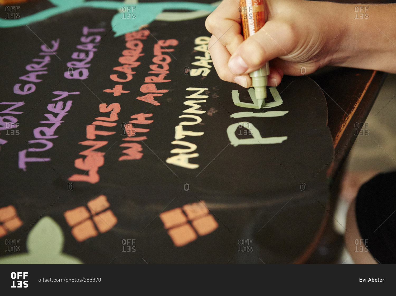 Child's hand writing a Thanksgiving menu on a chalkboard