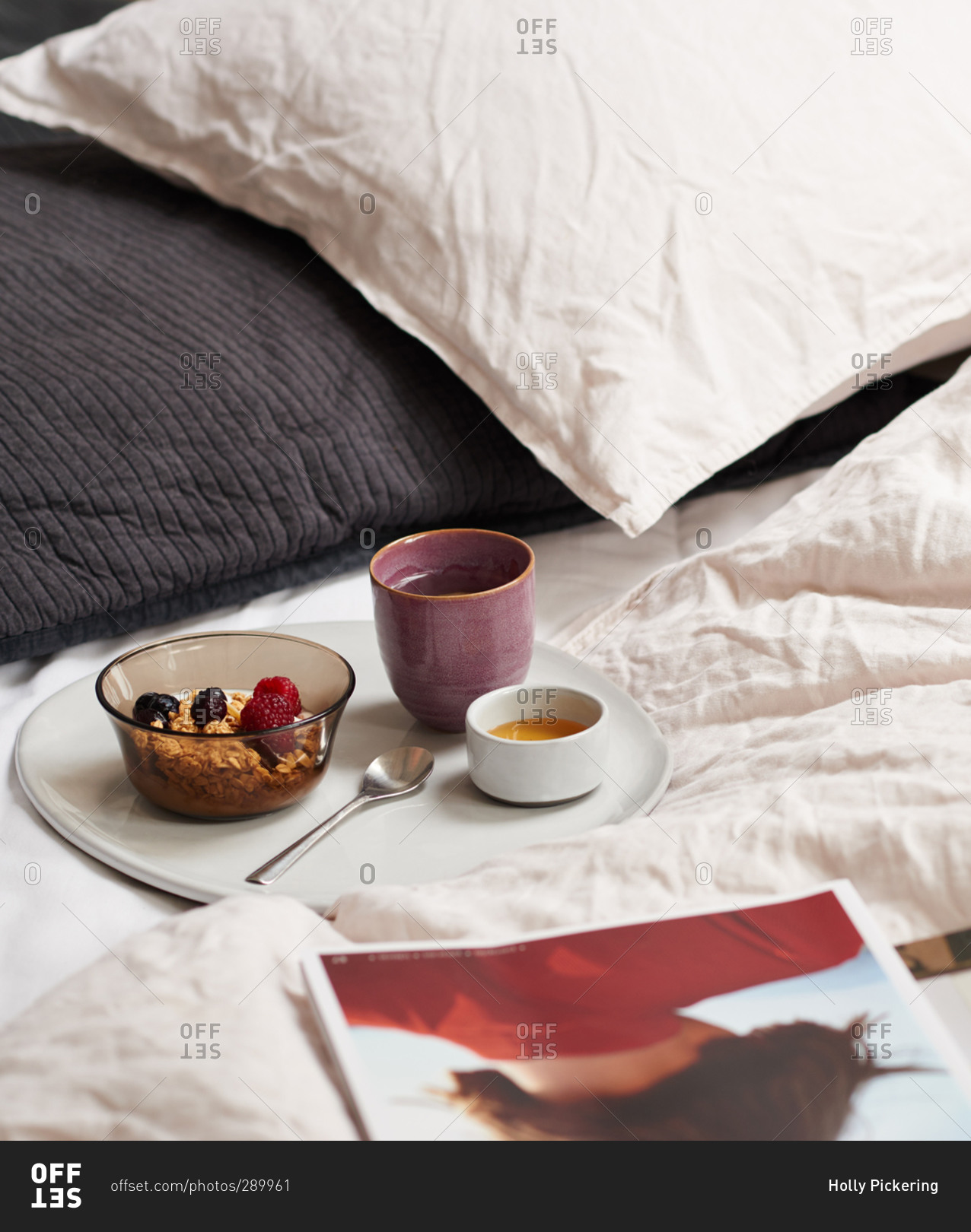 Breakfast tray of granola on a bed with bedding and pillows