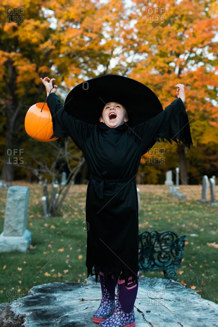 Girl dressed in a witch costume for Halloween standing in a cemetery