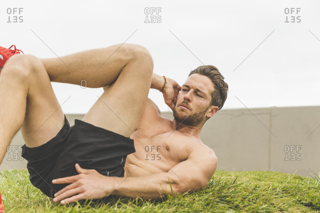 Shirtless athletic man doing a crunch twist during an outdoor workout