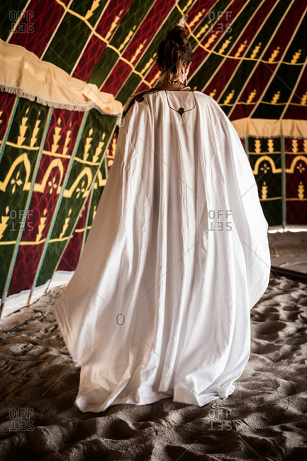 Back view of woman in a white robe inside a tent on sand