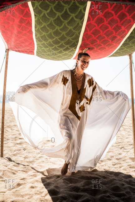 Happy woman in kaftan entering a tent on beach