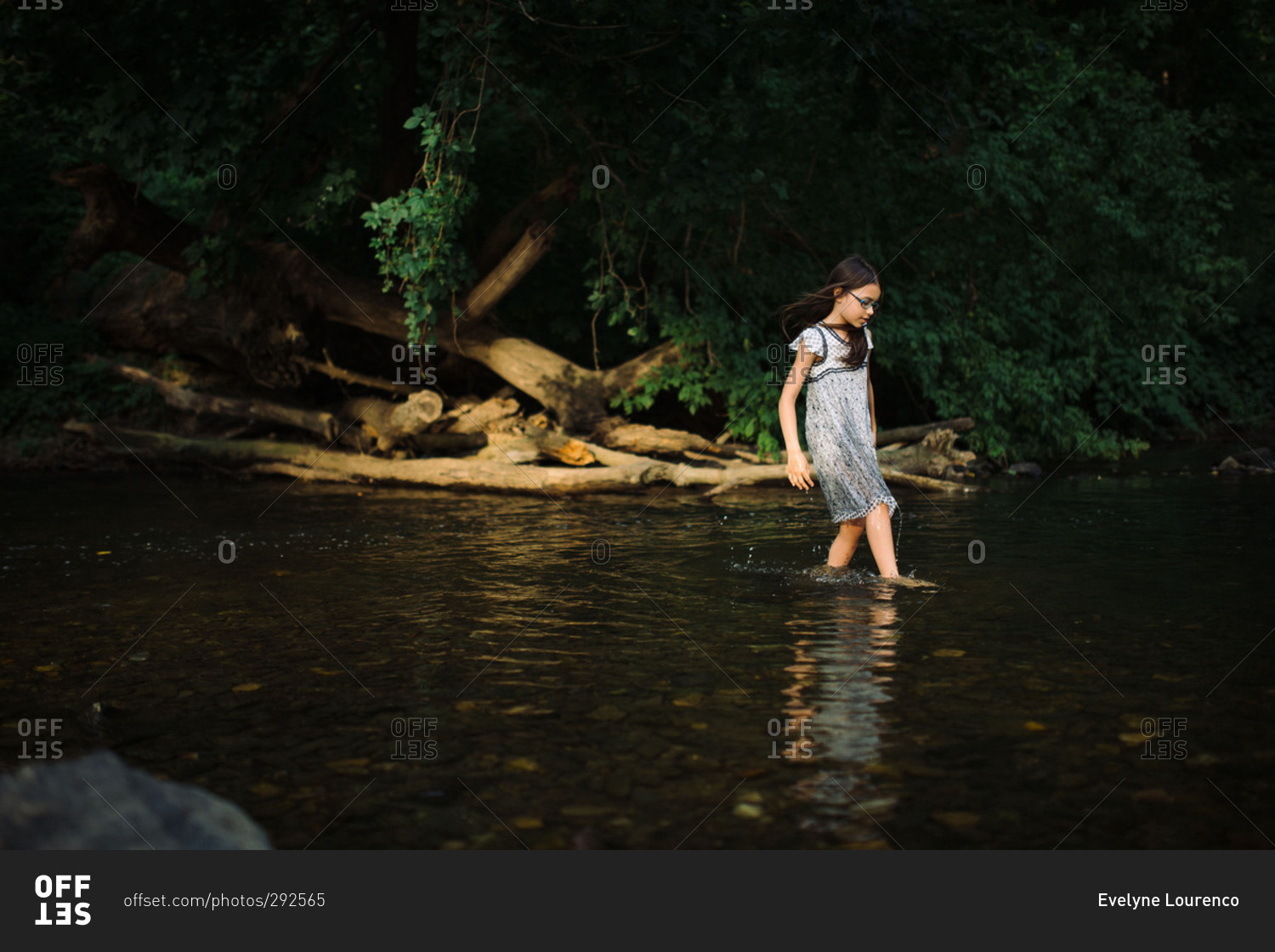 Girl in dress wading in river stock photo - OFFSET