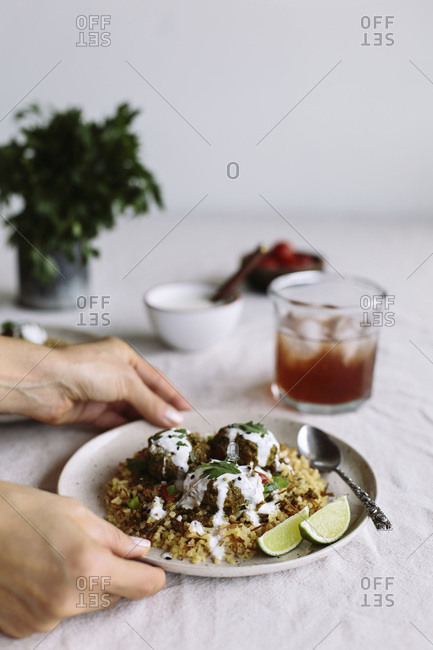Curried lentil meatballs served on bulgur pilaf and topped with yogurt sauce are served by a woman