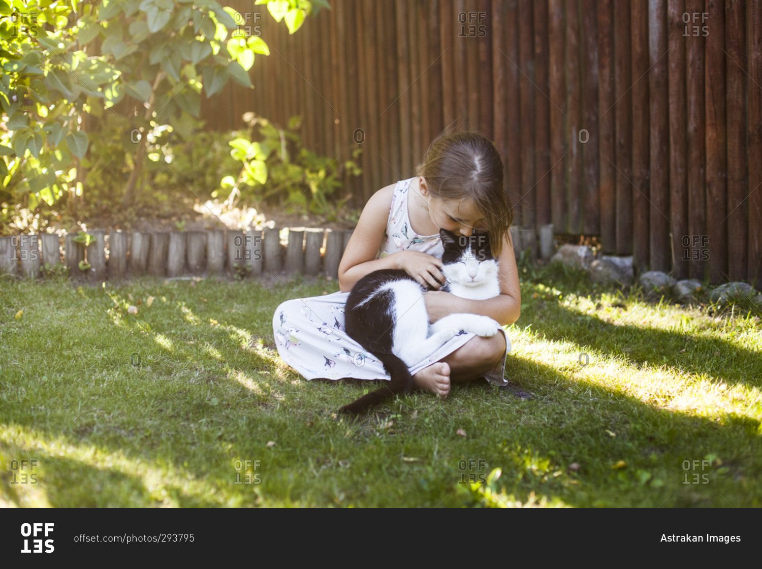 Young girl kisses her cat as she sits on grass in backyard