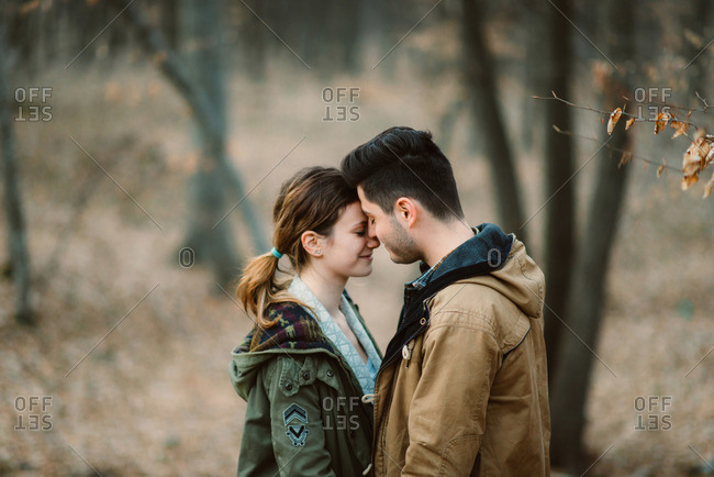 Couple standing in the woods touching foreheads.