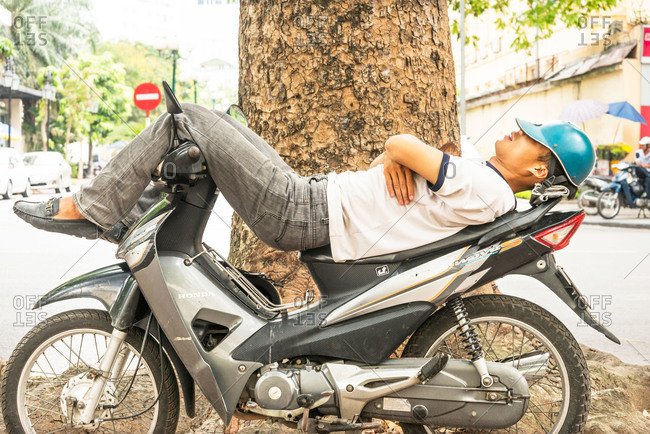 Hanoi, Vietnam - May 19, 2015: A very tired Vietnamese man laying on his motorbike and sleeping on a pavement in the city of Hanoi, Vietnam