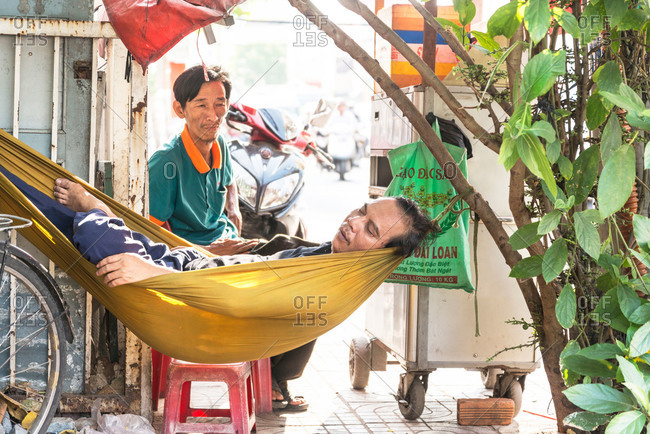 Saigon, Vietnam - April 21, 2015: A man lying in a hammock sleeping while his friend looks towards him in the city of Saigon, Vietnam