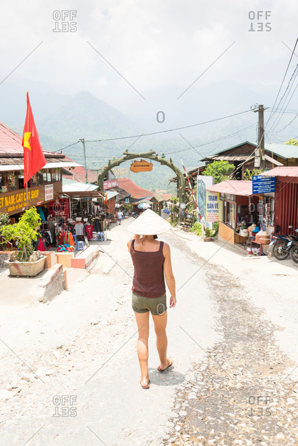 A female western tourist wearing a conical hat walks towards Cat Cat Village in the Sapa region of Northern Vietnam