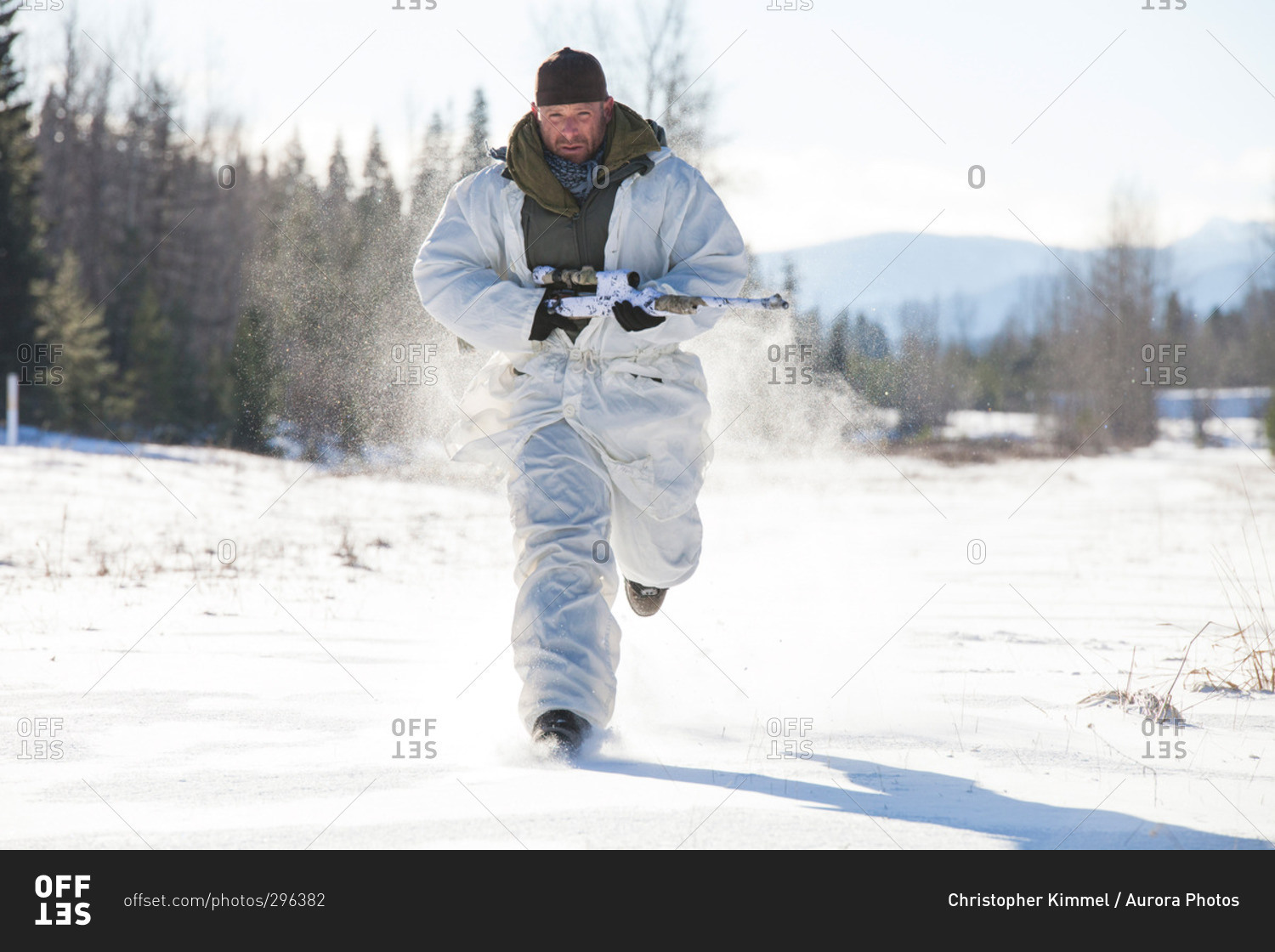 A hunter wearing a cold-weather camouflage outfit carries his rifle while running through a snow-covered field