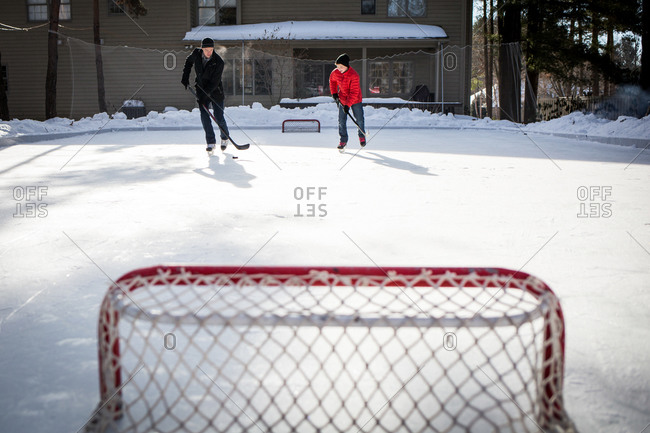 Man And Teenage Son Practicing Ice Hockey On Their Backyard Rink