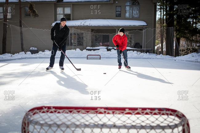 Father And Teenage Boy Practicing Ice Hockey On Backyard Ice Rink